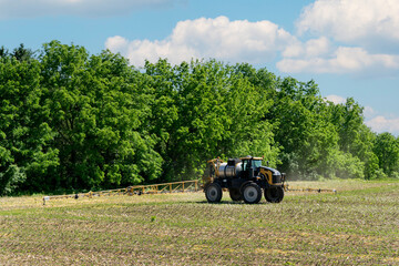 Tractor spraying pesticides/fertilizer on field with sprayer at spring