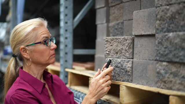 Attractive mature woman calculating on phone how man bricks she will need for backyard hardscaping home landscape improvement project.