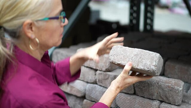 Attractive mature woman shopping looking at hardscaping bricks for home landscape improvement project.