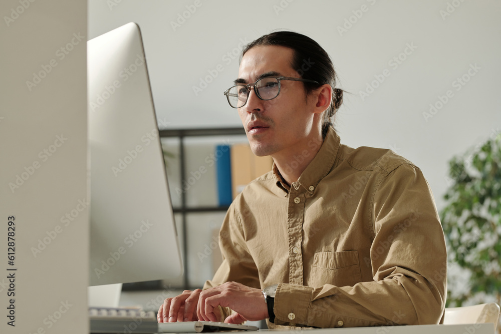 Poster young asian male entrepreneur looking at online financial data on computer screen while analyzing it