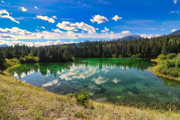 Fototapeta na wymiar Clouds scud across a bright blue sky and are reflected in the glassy waters of the lakes of the Valley of Five Lakes in the Jasper region of the Canada Rockies