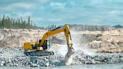 Yellow excavator placing stones in the bottom of an excavation