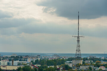 A huge modern TV tower rises above the roofs of residential buildings in the city center. Iron TV tower on the background of gray clouds during sunset.