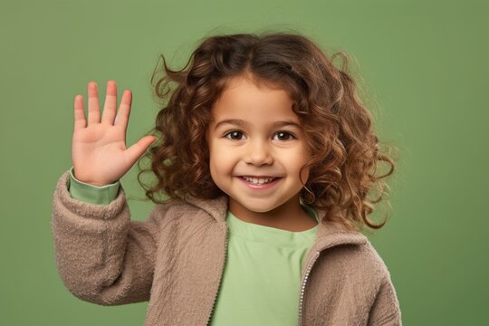 Headshot portrait photography of a tender kid female waving with the hand against a spearmint green background. With generative AI technology