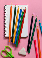 Notebook, colorful pencils, scissor and eraser on a pink background. Back to school concept.