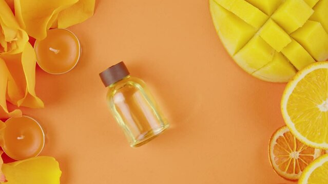 Jar of cosmetic oil perfume on the table . Composition of citrus slices, flowers, mango, aroma candles on orange background close-up, top view, zoom. Summer bright texture studio shot.