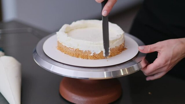 Woman in black apron smearing organic sugar free cake layers with delicious cream using kitchen utensil confectioner standing at table making custom pastry for wedding celebration