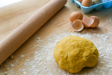 Ball of raw pasta dough with eggshells, egg carton, and rolling pin in the background