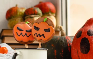Foto op Plexiglas Halloween cookies on a stick in a white cup surrounded by orange pumpkins near the window. © Tanya