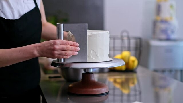 Professional confectioner spreading white sugar free mastic around baked cake with knife skilled woman in apron making delicious organic pastry for customer standing in kitchen