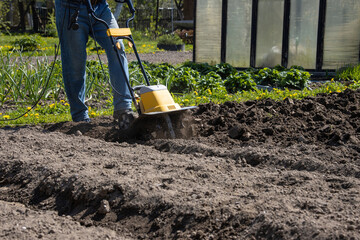 Loosening the soil in the garden beds with an electric hand-held cultivator