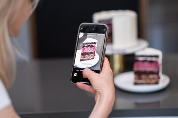 Hand of food blogger holding phone taking picture of piece of homemade shortcake on plate on...