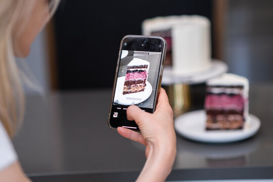 Hand of food blogger holding phone taking picture of piece of homemade shortcake on plate on kitchen table woman capturing finished pastry on camera to show on social media closeup