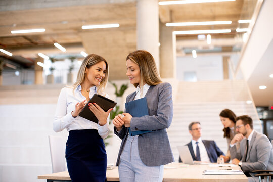 Two young business women looking at financial results on digital tablet in front of their team at the office