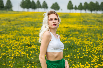 Naklejka na ściany i meble Young beautiful blonde woman posing in a spring field of dandelions