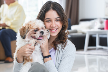 Portrait of Caucasian teenage girl playing with shih tzu puppy dog at home. Young beautiful woman sitting on floor, smiling, having fun holding little fluffy dog pet with love and care © Pruksachat