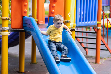 Adventurous preschooler with Down syndrome riding slide holding on to side barriers with hands...