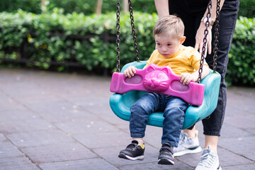 Curious little boy with Down syndrome riding on swings with help of mother caring parent...