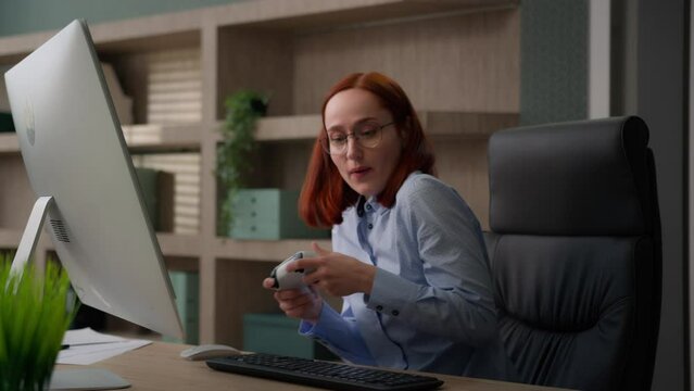 Funny female office worker addicted video game business woman playing console controller play online while nobody see girl businesswoman scared get caught hide joystick pretend working with computer