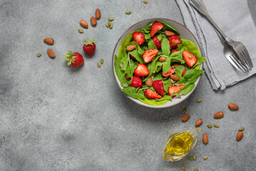 Summer salad with strawberries, arugula, spinach, seeds. Gray concrete background. Vegan and vegetarian food. Healthy food concept. Top view, flat lay, copy space