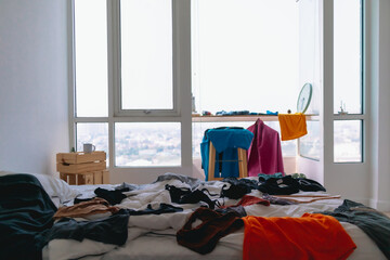 Cluttered and untidy apartment bed room full of colorful clothes on everywhere.