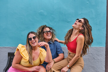 three young girl friends sitting on a bench laughing, having fun and enjoying themselves