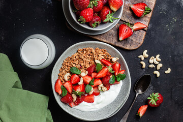 Granola with yogurt and strawberries in a plate on a dark background