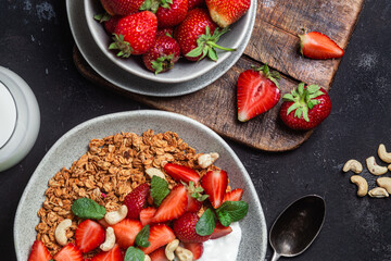 Granola with yogurt and strawberries in a plate on a dark background
