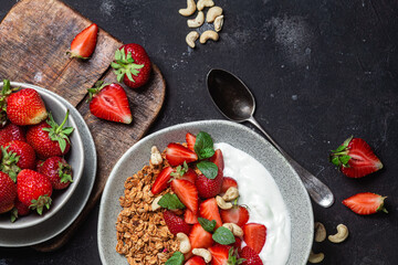 Granola with yogurt and strawberries in a plate on a dark background