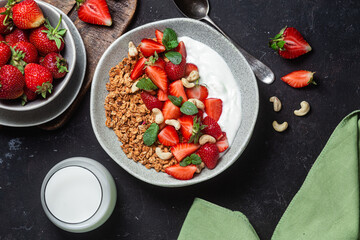Granola with yogurt and strawberries in a plate on a dark background