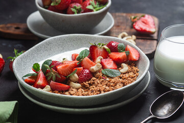 Granola with yogurt and strawberries in a plate on a dark background