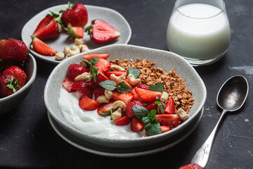 Granola with yogurt and strawberries in a plate on a dark background