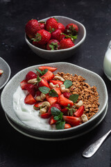 Granola with yogurt and strawberries in a plate on a dark background