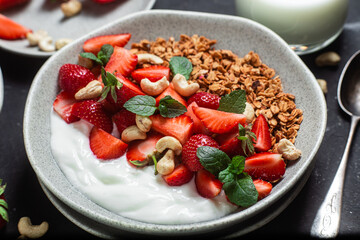 Granola with yogurt and strawberries in a plate on a dark background
