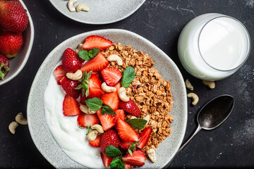 Granola with yogurt and strawberries in a plate on a dark background