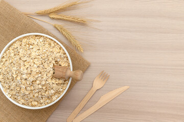 Oatmeal flakes in a white bowl with ears of wheat. Scoop wooden.