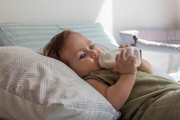 Bebé de ocho meses tomando su leche en su biberón en su cuarto en un día soleado.