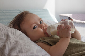Bebé de ocho meses tomando su leche en su biberón en su cuarto en un día soleado.