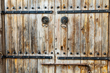 A part of old worn looking wooden door with black wrought iron trim, slider and handles close up...