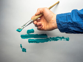 Paintbrush in hand on white background. Painting in the studio. Painting in process. Handmade. Hand of an artist on white background.