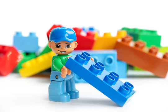 Lego man from Lego Duplo holding a blue Lego brick on the background of colorful building blocks