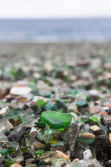 A unique glass bay in Vladivostok, Russia. Vertical photo.Sea-polished green glass on the beach against the background of the Sea of Japan