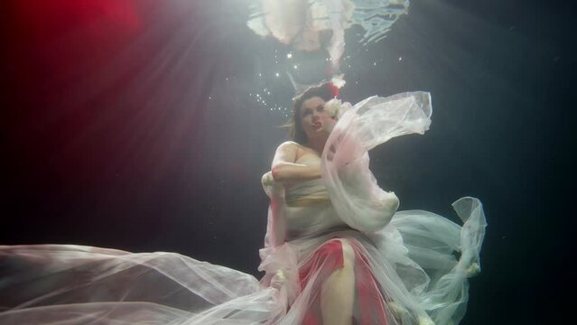 romantic underwater portrait of beautiful brunette woman swimming in depth, slow motion