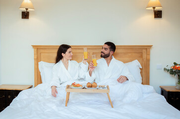 Couple Clinking Glasses With Juice In Bed In Hotel Bedroom