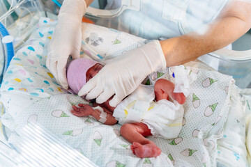 Obraz na płótnie Canvas Top view of unrecognizable doctor in white gloves carying at neonatal intensive care unit in hospital. Newborn is placed in the incubator.