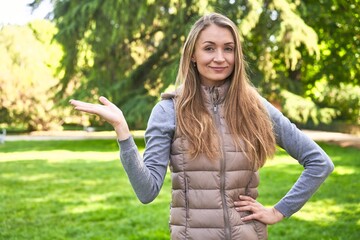 Middle-aged woman in a park on a sunny day laughs out loudly keeping hand on chest.