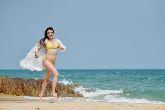Joyful young woman having fun on sandy beach, running and jumping