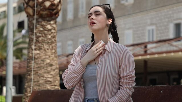 Young Caucasian suffering woman is sitting on bench fanning herself and wipes sweat of high hot temperature. Summer season. Concept of overheating, thirst and sunstroke