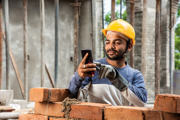 Happy smiling young indian construction labour busy on mobile phone at workplace