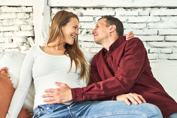 A blissful couple, both 40, expecting a baby, radiates joy on their cozy sofa at home.